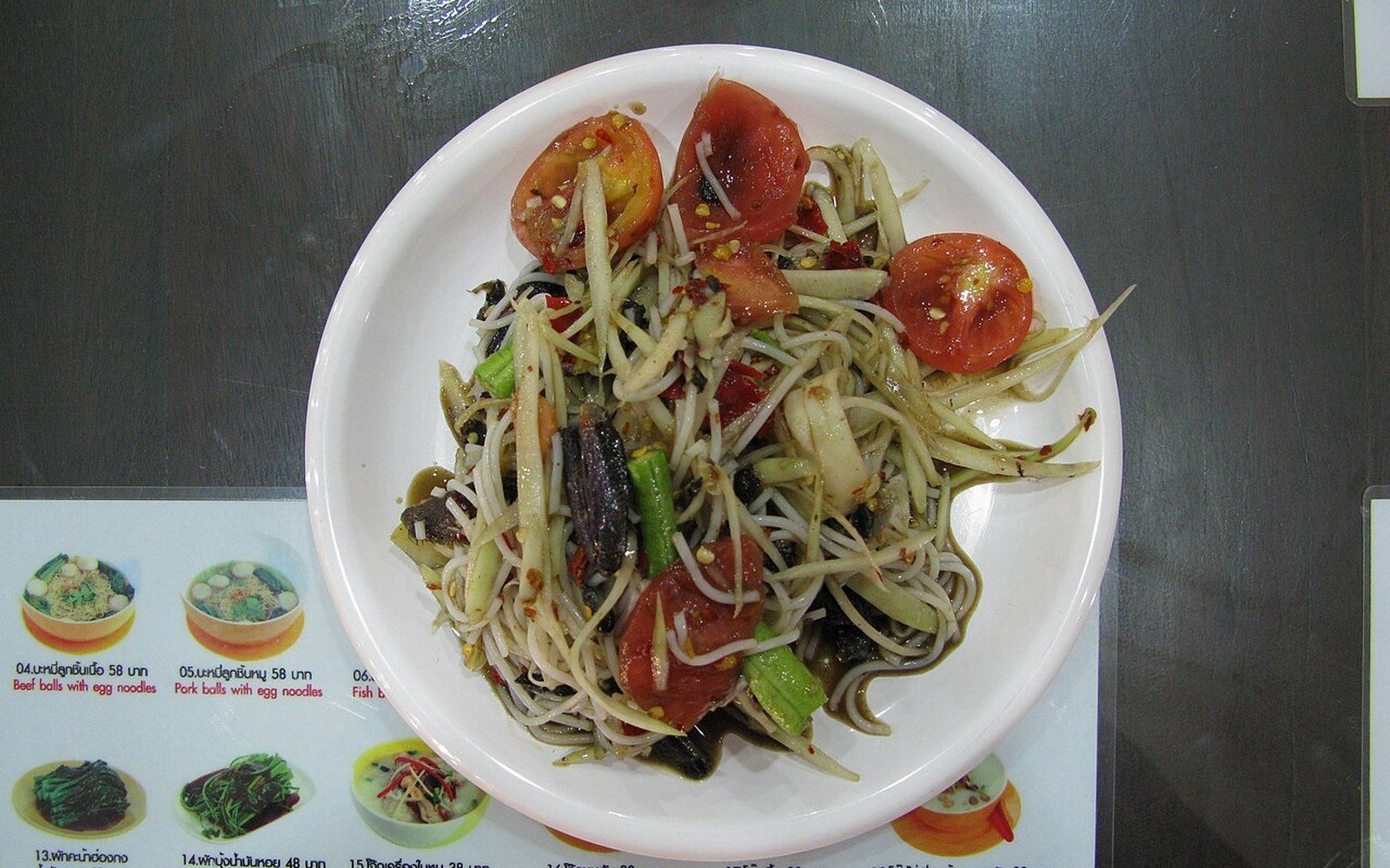 Green papaya salad with tomatoes and preserved crab on a white plate